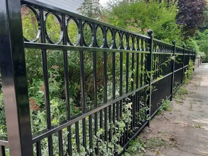 Modern zwart sierhekwerk met verticale spijlen en decoratieve cirkelornamenten, afgewerkt met bolornamenten op de staanders.