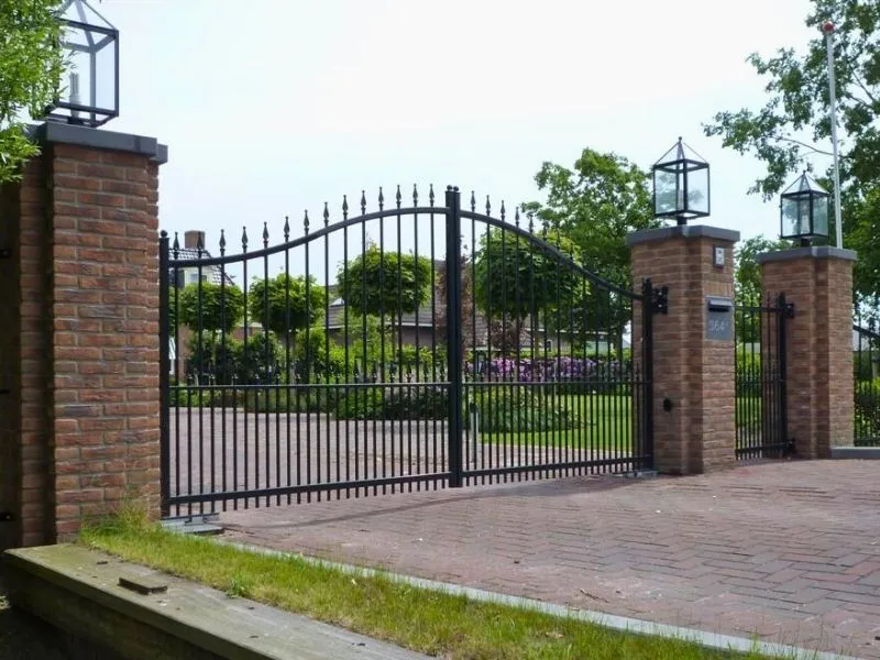 Modern zwart sierhekwerk met dubbele poort, verticale spijlen, sierpunten en gebogen bovenlijn, geplaatst tussen gemetselde kolommen