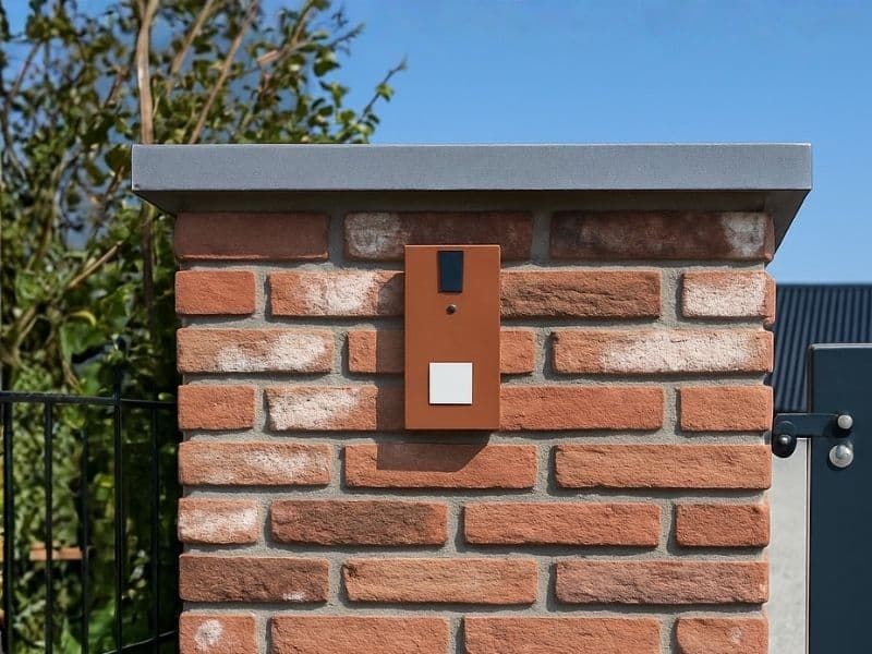 Moderne intercom op gemetselde poer voor toegangshek, uitgevoerd in roestkleurig designpaneel