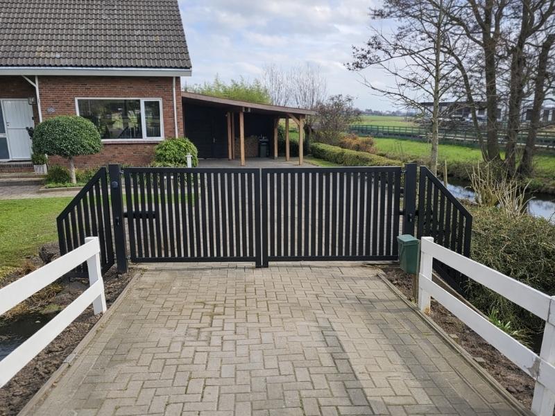 Dubbele draaipoort van staal bij oprit, voor veilige toegangscontrole en afsluiting van erf bij woning met hekwerk.
