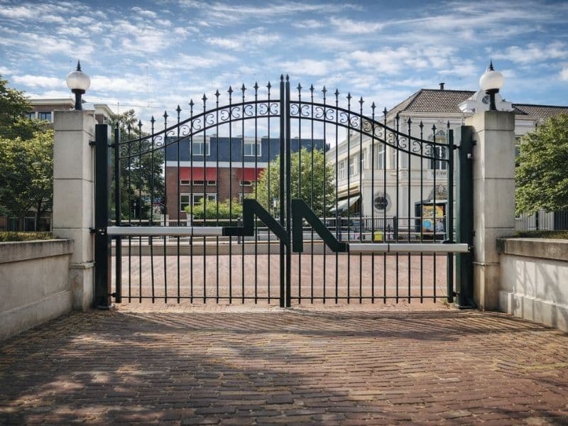 Elektrische draaipoort van sierstaal bij entree, voor automatische toegangscontrole en veilige afsluiting van terrein met hekwerk.