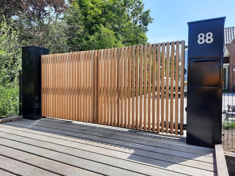 Houten en stalen draaipoort bij oprit met brievenbuszuil, voor toegangscontrole en moderne afsluiting van erf met hekwerk.