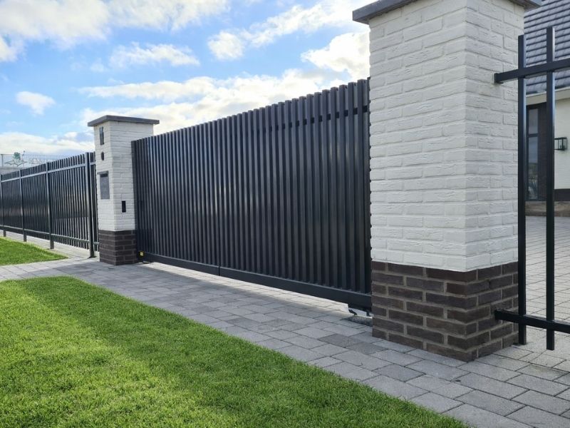 Houten schuifpoort bij oprit met hekwerk en zuilen, voor toegangscontrole en moderne afsluiting van woning of terrein.