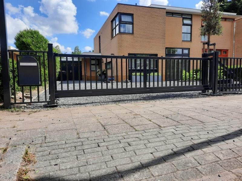 Schuifpoort bij oprit van woning met hekwerk, voor toegangscontrole en veilige afsluiting van erf met moderne uitstraling.