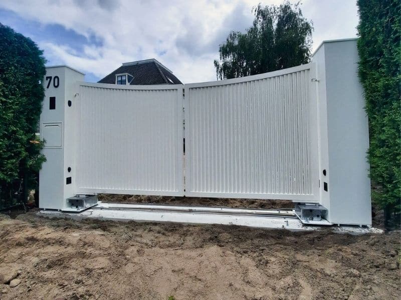 Witte lamellen draaipoort in Noordwijk met dubbele vleugels en moderne poerzuilen bij een woning.