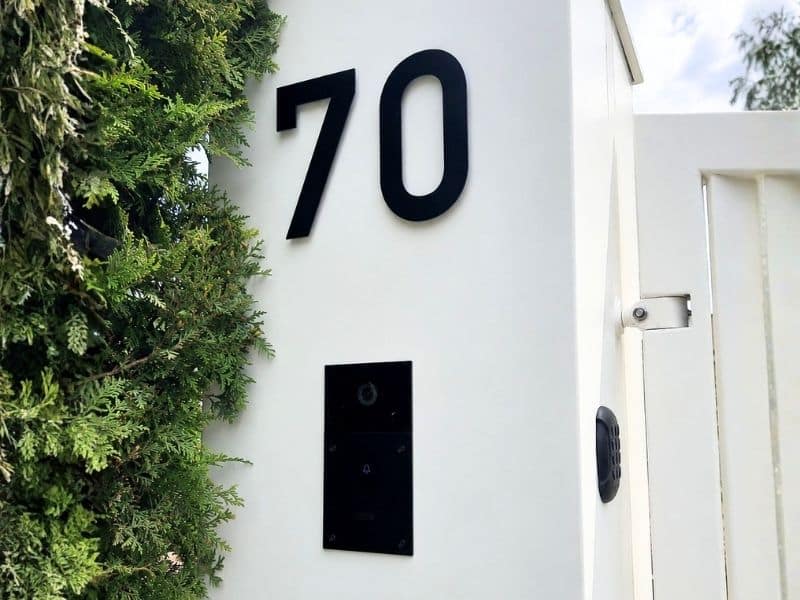 Witte lamellen draaipoort met intercom in Noordwijk, met zwarte intercom en huisnummer op witte poerzuil.