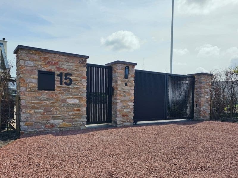 Poort onderhoud van een moderne elektrische toegangspoort bij een woning met stenen zuilen.